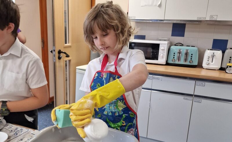 primary school boy washing dishes for a school event which is part of school life in england